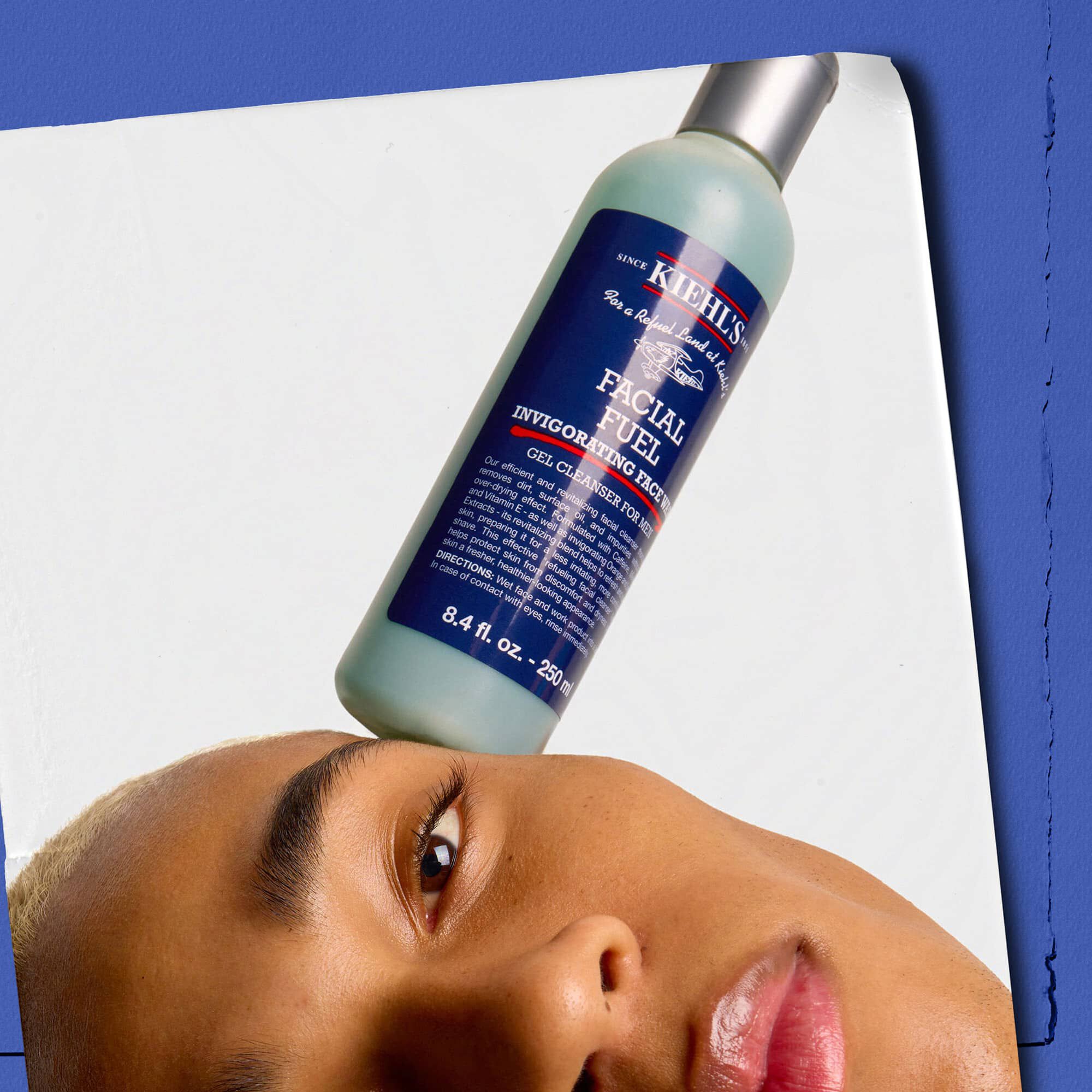 Model with a bottle of Kiehl's Facial Fuel Energizing Face Wash balanced on their face