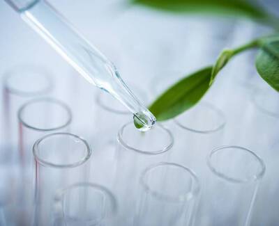 A dropper releasing a liquid drop above a row of test tubes, with a green leaf nearby.