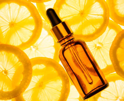 A brown dropper bottle lies on a background of bright yellow lemon slices.