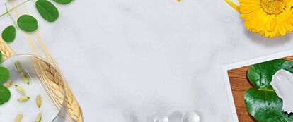 A flat lay arrangement featuring natural ingredients like olive branches, flowers, and green leaves alongside glassware and a marble surface, creating a fresh and inviting aesthetic.