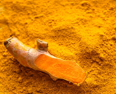 A piece of fresh turmeric root on a pile of bright yellow turmeric powder.