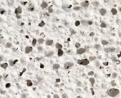 Close-up of a textured surface resembling porous white material, featuring numerous small holes and variations in texture.