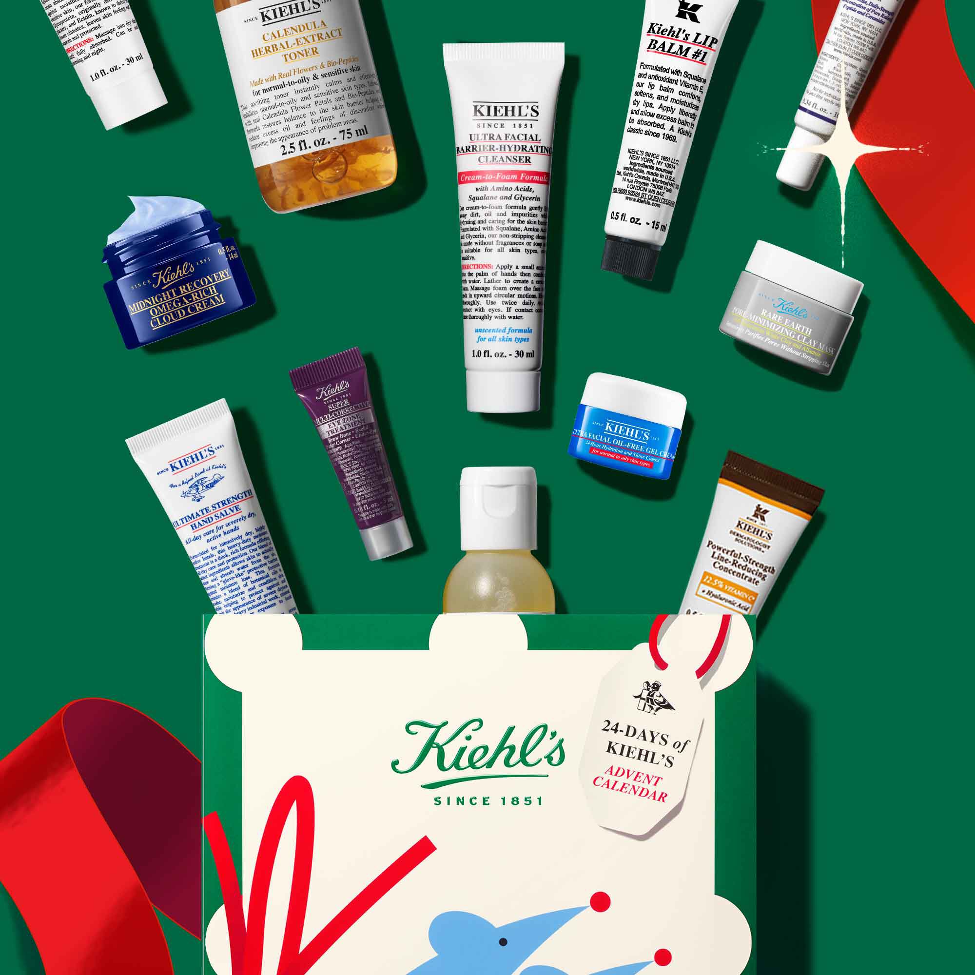 Hands hold a Kiehl’s holiday gift box with colorful abstract design, logo, and “Since 1851” tag on a festive green background.