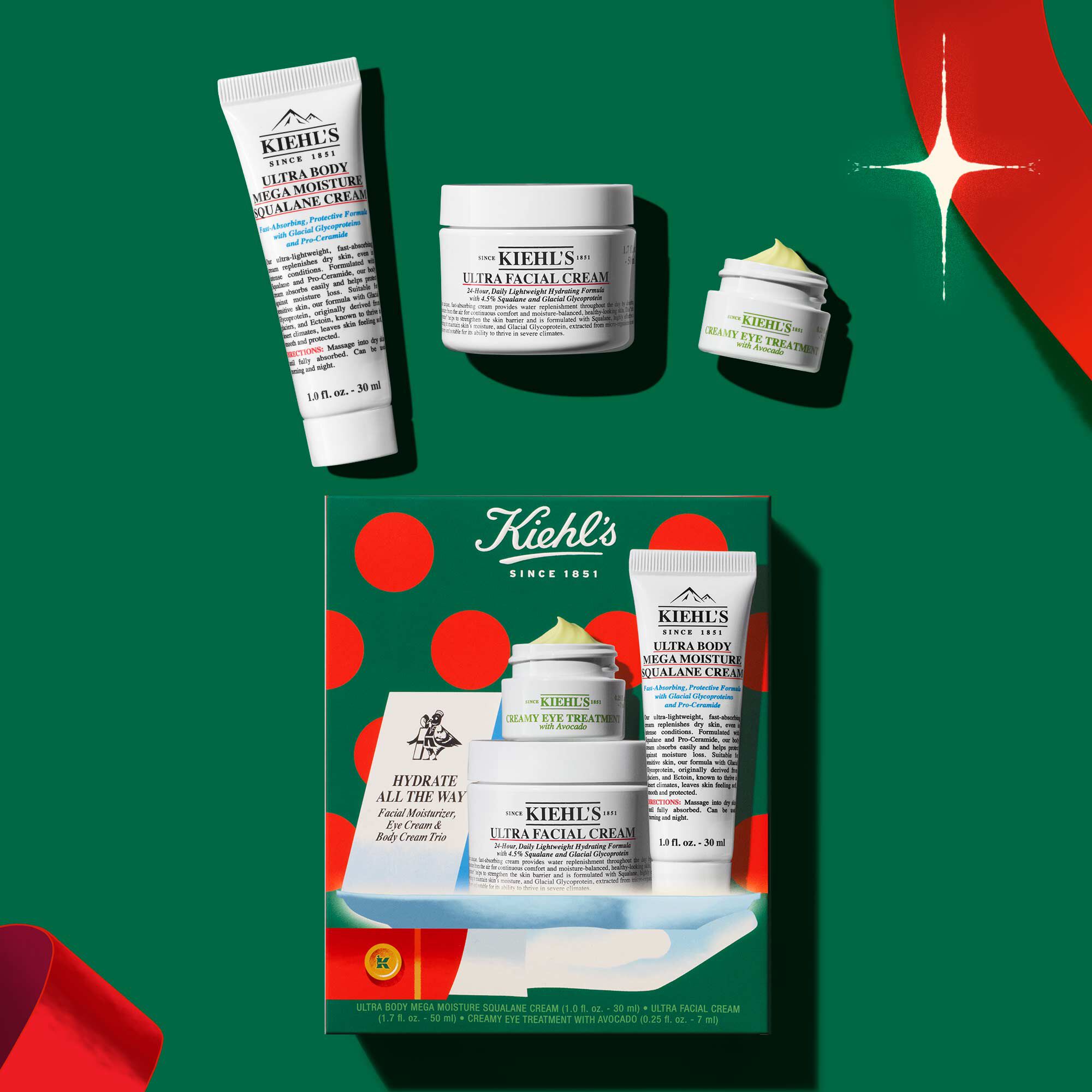 Kiehl's holiday skincare gift set featuring Ultra Facial Cream, Creamy Eye Treatment with Avocado, and Ultra Body Mega Moisture Squalane Cream arranged on a festive green background.​