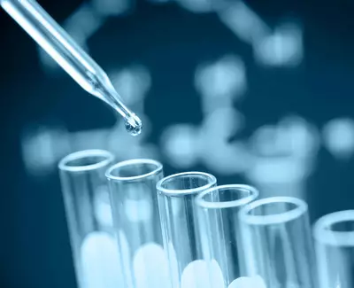 A dropper releasing a drop of liquid into several test tubes, with a blurred background of a DNA strand diagram.