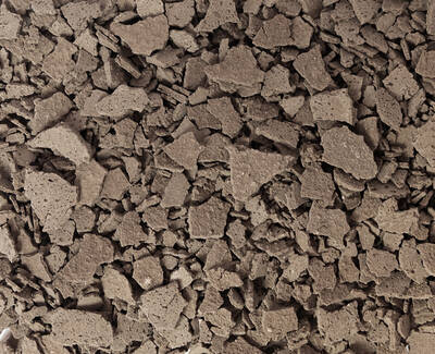 A close-up view of irregularly shaped, broken pieces of a textured brown material, resembling crumbled rock or soil.