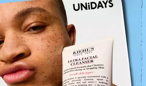 Promotional image featuring a Kiehl's branded pouch filled with skincare products,  Ultra Light Daily Defense Aqua Gel SPF50 5ml, Calendula Toner 40ml, Rare Earth Mask 14ml, Micro Dose Retinol Treatment 4ml, Facial Fuel Moisturiser 15ml, Creme De Corps Body Lotion 30ml, Clearly Corrective Dark Spot Solution 4ml- on a pink background.