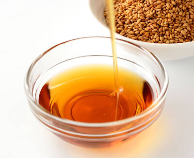 A glass bowl containing golden-brown oil, with sesame seeds in a white bowl in the background.