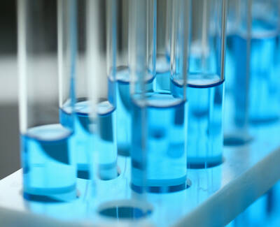 A close-up view of several test tubes filled with bright blue liquid, arranged in a rack with a soft blue glow from below.