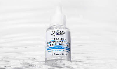 A clear glass dropper bottle of Kiehl's Ultra Pure High-Potency Serum, labeled with "15% Hyaluronic Acid" and "Moisture-Plumping," set against a reflective, watery background.