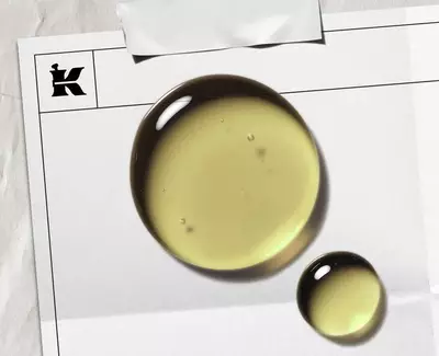 A sliced avocado revealing its pit alongside a small bowl of golden avocado oil, placed on a wooden surface.