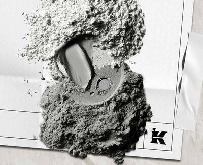 A close-up of various shades of gray powders and a cream-like texture on a crumpled white surface, featuring a stylized 'K' logo.