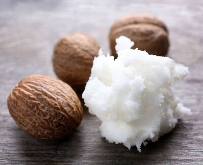 A cluster of whole nutmeg seeds and a mound of white, fluffy nutmeg powder on a wooden surface.