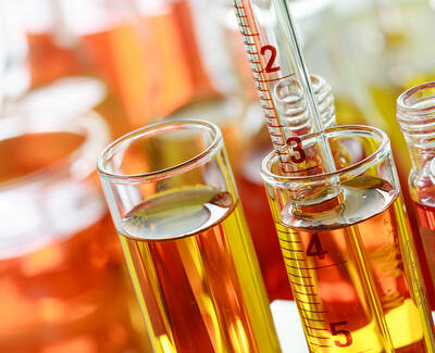 Close-up of test tubes and a graduated cylinder filled with colorful liquids ranging from yellow to orange, arranged on a blurred background.