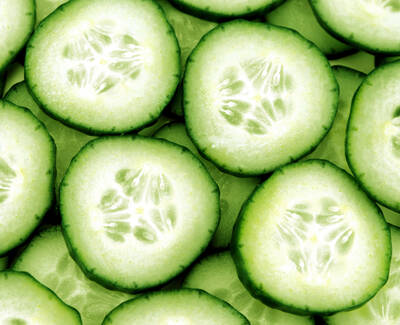 A close-up view of fresh cucumber slices arranged in a uniform pattern, showcasing their vibrant green skin and light green flesh.