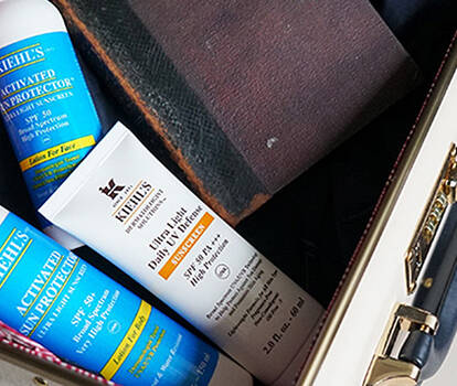 A stylish bag contains skincare products, including a shampoo and a facial moisturizer, alongside a small book. The interior of the bag features a vibrant patterned lining.