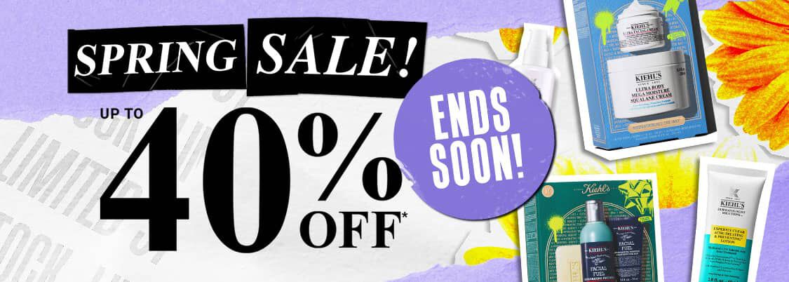 Promotional graphic for the Kiehl’s Spring Sale. Centered on the left is large, bold text reading ‘SPRING SALE!’ in white on black tape-style backgrounds, with ‘UP TO 40% OFF*’ in a classic serif font below. The background is a textured, light purple and white paper collage with a bright yellow flower in the corner. Scattered on the right are Kiehl's skincare products and gift sets, including the Ultra Facial Cream, Ultra Body Mega Moisture Squalane Cream, Facial Fuel Energizing Face Wash, and Expertly Clear Acne-Treating Lotion. The visual style is a modern, high-contrast collage with a mix of gritty 'street' elements and clean apothecary product shots.