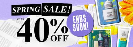 Promotional graphic for the Kiehl’s Spring Sale. Centered on the left is large, bold text reading ‘SPRING SALE!’ in white on black tape-style backgrounds, with ‘UP TO 40% OFF*’ in a classic serif font below. The background is a textured, light purple and white paper collage with a bright yellow flower in the corner. Scattered on the right are Kiehl's skincare products and gift sets, including the Ultra Facial Cream, Ultra Body Mega Moisture Squalane Cream, Facial Fuel Energizing Face Wash, and Expertly Clear Acne-Treating Lotion. The visual style is a modern, high-contrast collage with a mix of gritty 'street' elements and clean apothecary product shots.
