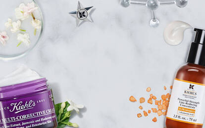 A flat lay of skincare products on a marble surface, featuring two bottles and a purple jar, surrounded by natural elements like flowers and orange peels.