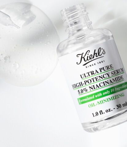 A bottle of Kiehl's Ultra Pure High-Potency Serum with a dropper, resting on a white marble surface, accompanied by a few droplets of the serum.
