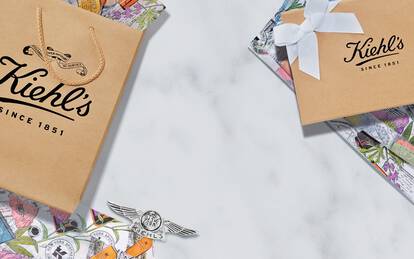 A flat lay image featuring Kiehl's gift bags and wrapped packages on a marble surface, complemented by colorful illustrations and a photo of Kiehl's staff in the center.