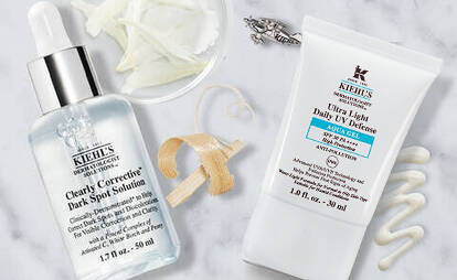 A flat lay of skincare products from Kiehl's, featuring a dropper bottle and a tube, arranged on a marble surface with some accessories and skincare elements in the background.